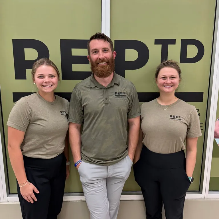 Three members of the REPTD athletic training staff in front of the REPTD banner